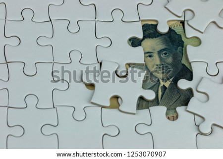 Japanese 1,000 Yen banknote hiding under blank white puzzle jigsaw for economic business concept