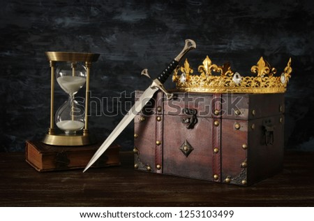 low key image of beautiful queen/king crown, vintage hourglass and sword. fantasy medieval period