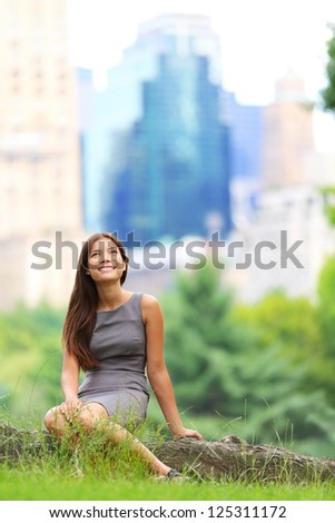 Young Asian Business woman in New York Central Park. Businesswoman looking up at copy space with skyscraper buildings from New York skyline in background. Young female professional. Mixed race.