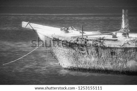 Black and white old sailboat on the water tied to a dock with ropes and barnacles resting in a marina. Royalty-Free Stock Photo #1253155111