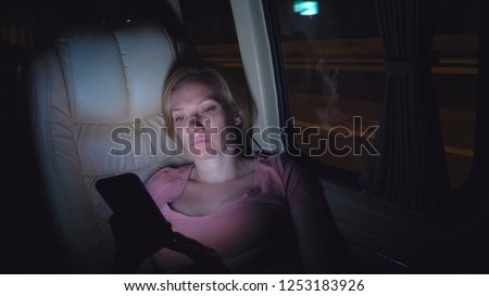 A tired woman rides the night on the bus, use her phone.