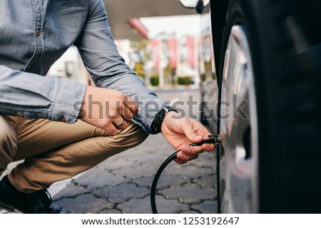 Close up of man crouching on the gas station and inflating tire. Royalty-Free Stock Photo #1253192647