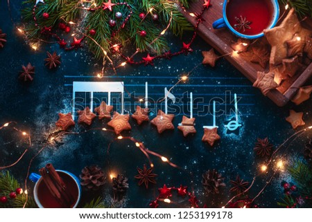 Christmas melody notes flat lay with star-shaped cookies, fir tree branches, wooden tray, anise stars, and decorations. Christmas carol concept for a header or postcard