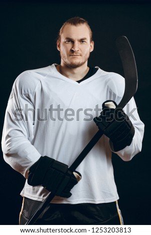 Handsome caucasian hockey player posing with gaming stick at studio, looking at camera with confident look, isolated over black background. Smiling at camera isolated, over black background