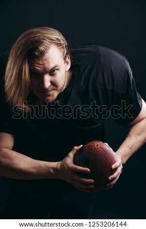 Emotional shot of caucasian football player in black safety jersey but without helmet, prepares to pass the ball, with his hair waving on air