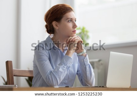 Lost in thoughts woman sits at workplace desk in office in front of laptop holds hands on chin looking away thinking about working moments. Businesswoman planning or trying solve some business issues Royalty-Free Stock Photo #1253225230