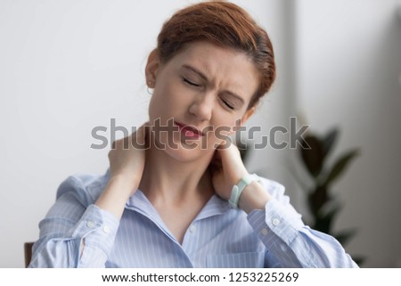 Head shot woman writhing in pain suffering from neck pain at work in office. Fatigued female touching massaging sore neck feels unhealthy. Sedentary lifestyle, long time working without break concept Royalty-Free Stock Photo #1253225269