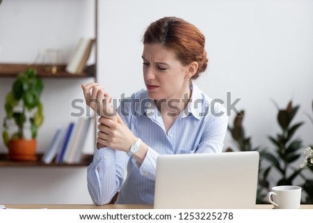 Businesswoman sitting at desk in office touch wrist feels pain. Unhealthy upset female having carpal tunnel syndrome because of active and long-term use of the keyboard and mouse in the wrong posture Royalty-Free Stock Photo #1253225278