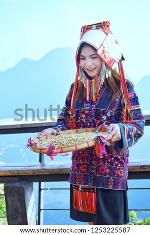 Asian girl in Akha tribal costume and a basket of coffee beans with mountain views at Coffee shop on mountain at Doi Pha Hee, Mae Sai, Chiang Rai, the northernmost of Thailand.