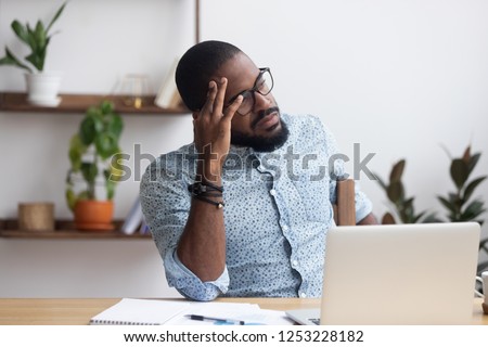 Serious african millennial businessman thinking cogitating about business issues. Frustrated black entrepreneur searching problem solution sitting alone on chair at modern office desk looking away Royalty-Free Stock Photo #1253228182