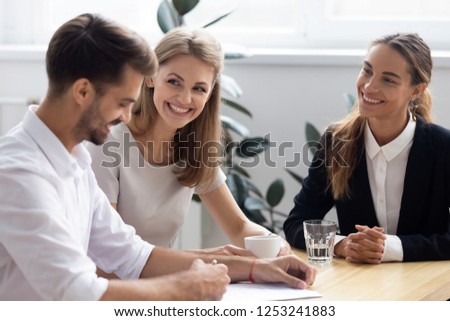 Businessman filling agreement form make deal during meeting with businesswomen company representatives. Happy job candidate HR managers sitting together at desk while man signing employment contract