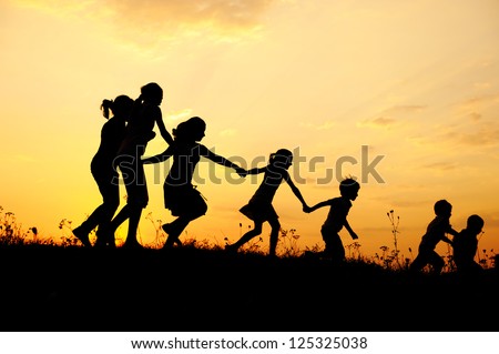 Several happy children running on meadow at summer sunset