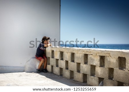 Boy leaning on retaining wall; admiring sea; Crete; Greece