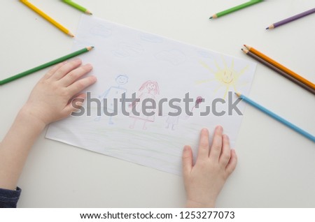 A child draws his family with pencils. Child's drawing and colored pencils. Family drawing on a white paper. Top view . Flat lay