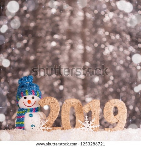 Happy smiling snowman and new year inscription 2019 on bright background with bokeh effect