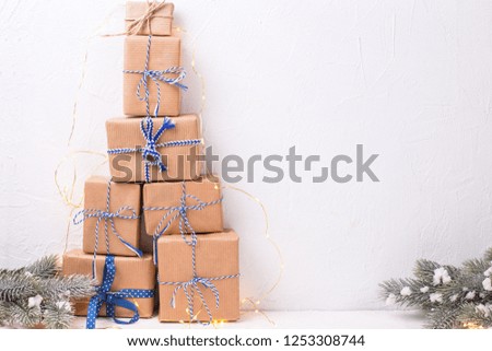 Stack of wrapped boxes with presents, fir tree branches and fairy lights on white textured background. Selective focus. Winter holiday, Christmas, New Year. Place for text.