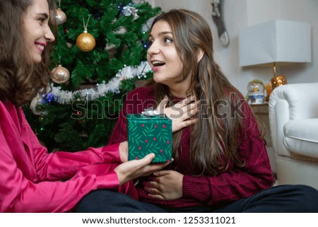 Beautiful young women sitting near Christmas tree at home exchanging with presents having fun