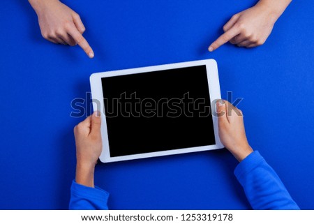 Kid hands pointing to white tablet computer in kid hands over blue background
