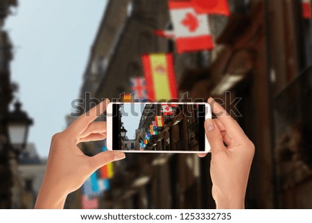 A tourist is taking a photo of flags of various world countries are hung out on one of the buildings in Italy on a mobile phone