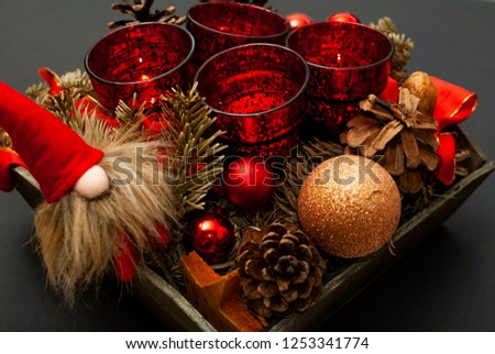 Close up of Advent wreath with four candles, fir tree, christmas balls, a dwarf and a fir cone on black background