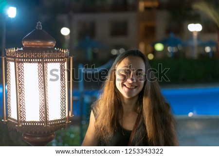Young woman near a large lantern on the background of a night hotel