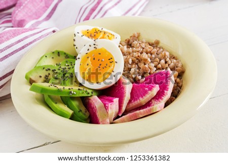 Buckwheat porridge buddha bowls with avocado, boiled eggs and  watermelon radish on white table. Healthy breakfast.