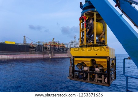 A Remoted Operated Vehicle (ROV) hanging on Launch & Recovery System (LARS) for underwater pipeline survey and inspection nearby Floating Storage Offloading (FSO) vessel. Royalty-Free Stock Photo #1253371636