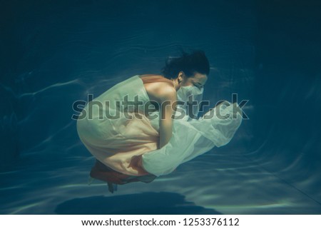 elegant slender girl swims underwater like a free diver in a white evening dress with beautiful fabric