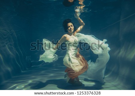 elegant slender girl swims underwater like a free diver in a white evening dress with beautiful fabric