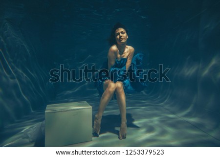 elegant pretty woman swims underwater like a free diver in a blue evening dress alone