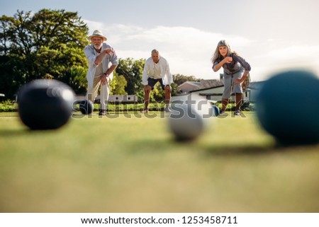 Senior man and woman playing boules competing with each other. Ground level shot of elderly people playing boules in a park with blurred boules in the foreground. Royalty-Free Stock Photo #1253458711