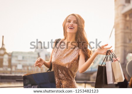Portrait of the happy divine young woman who is standing outdoors and holding the shopping bags in hands