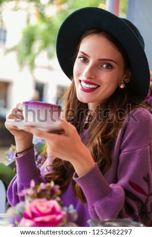 Portrait of the elegant, smiling young woman who is sitting in the restaurant outdoor and drinking a cup of tea