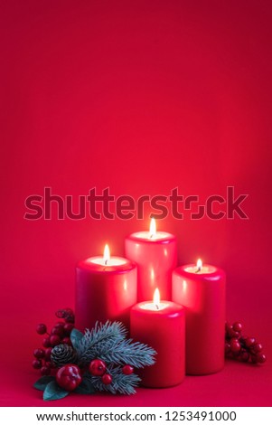 Four red burning advent candles, a green spruce branch on a red background, toned