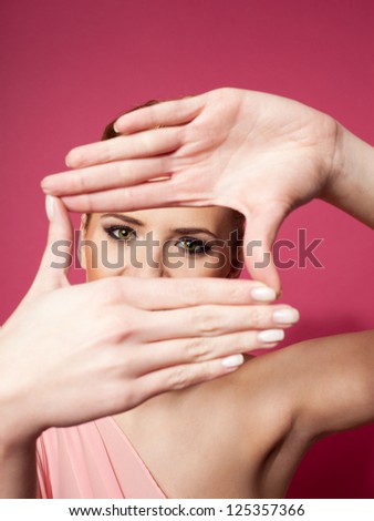 Portrait of  young woman creating a frame with her hands. Isolated on pink background.