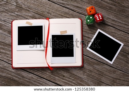 Blank instant photos, playing cubes and notebook on wooden background