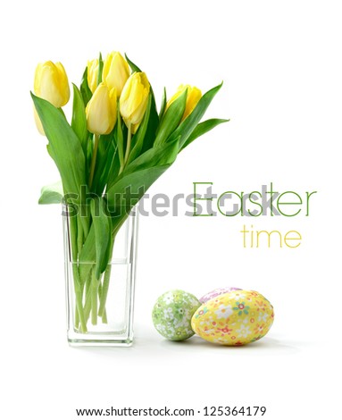 Studio macro of yellow tulips (Tulipa gesneriana) in a glass vase with decorative paper covered easter eggs against a white background. Copy space.