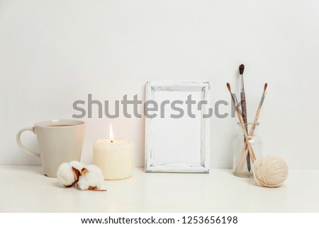 Vertical frame mockup with coffee cup, candle near white wall. Empty frame mock up for presentation design. Template framing for modern art. Hygge scandinavian style workspace. Natural eco home decor