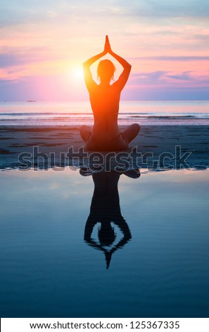 Young woman practicing yoga on the beach at sunset (with reflection in water)