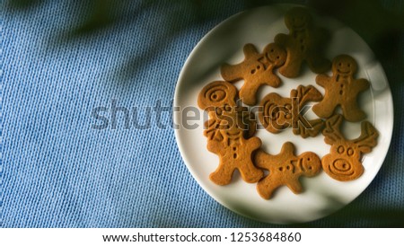 white plate with christmas gingerbread cookies through christmas tree branches on blue background