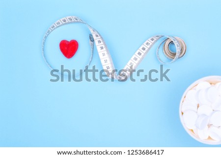 Conceptual background on the pharmaceutical theme on a blue background.Copy space for text.Magnetic measuring tape, red heart and pills.
