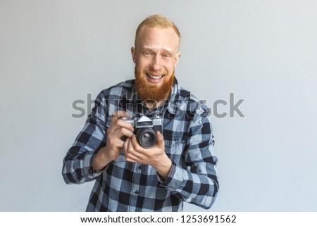 Red hair mature man standing isolated on grey wall holding film camera taking photos laughing cheerful