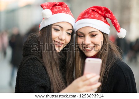 Smiling young women in Christmas hat using a smartphone together