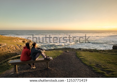 Couple enjoys beautiful coastal scenery near Dunedin in New Zealand. Romantic couple goes on holiday. A pair of couple goes on honeymoon in natural landscape. Happiness image of a young couple. Royalty-Free Stock Photo #1253771419