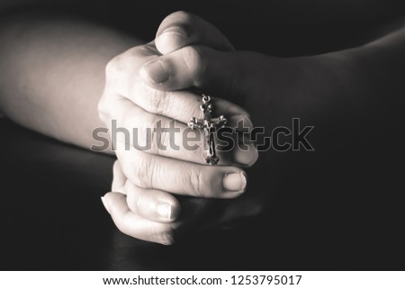 Hands praying holding a rosary with Jesus Christ in the cross.