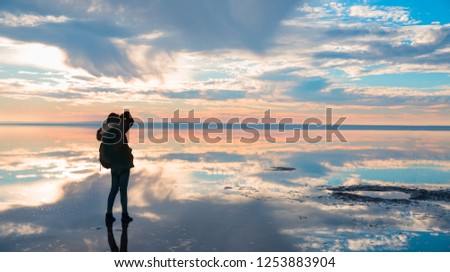 Silhouette of lone woman takes a picture of a sunset reflected in waters of salt lake, Ankara