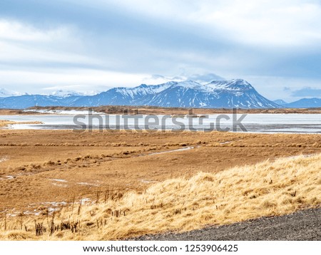 Field with snow in winter season with moutains in background under cloudy blue sky in Iceland
