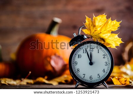 Vintage alarm clock and maple tree leaves with pumpkins on yellow wooden background with bokeh. Autumn season image style for Thaksgiving holiday