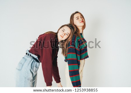 Two sisters twins beautiful girls hipsters in casual clothing look at camera on grey background isolated