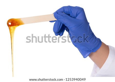 Beauticians hand with blue glove holding a spatula for wax